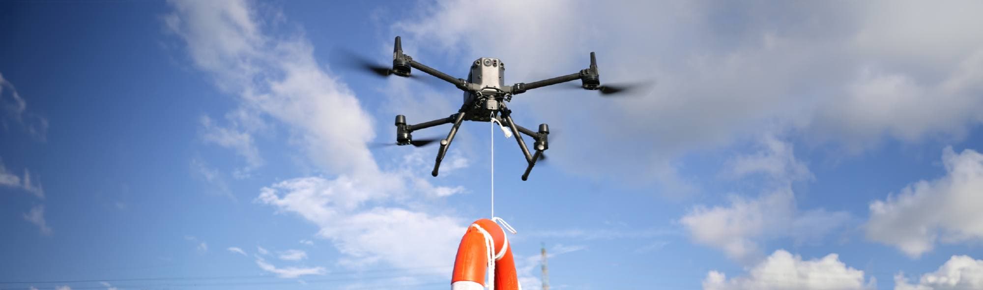 En drönare svävar i luften och bär en livboj under en klarblå himmel.