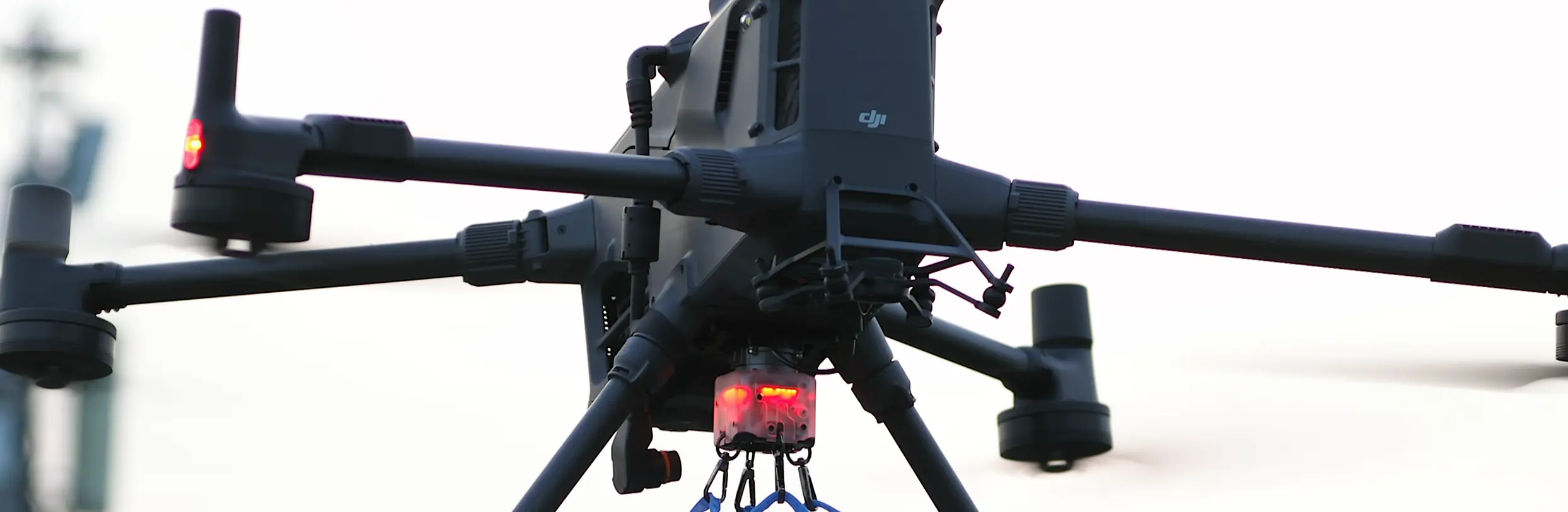 En drönare med flera rotorer svävar i luften, utrustad med en lysande röd lampa undertill.