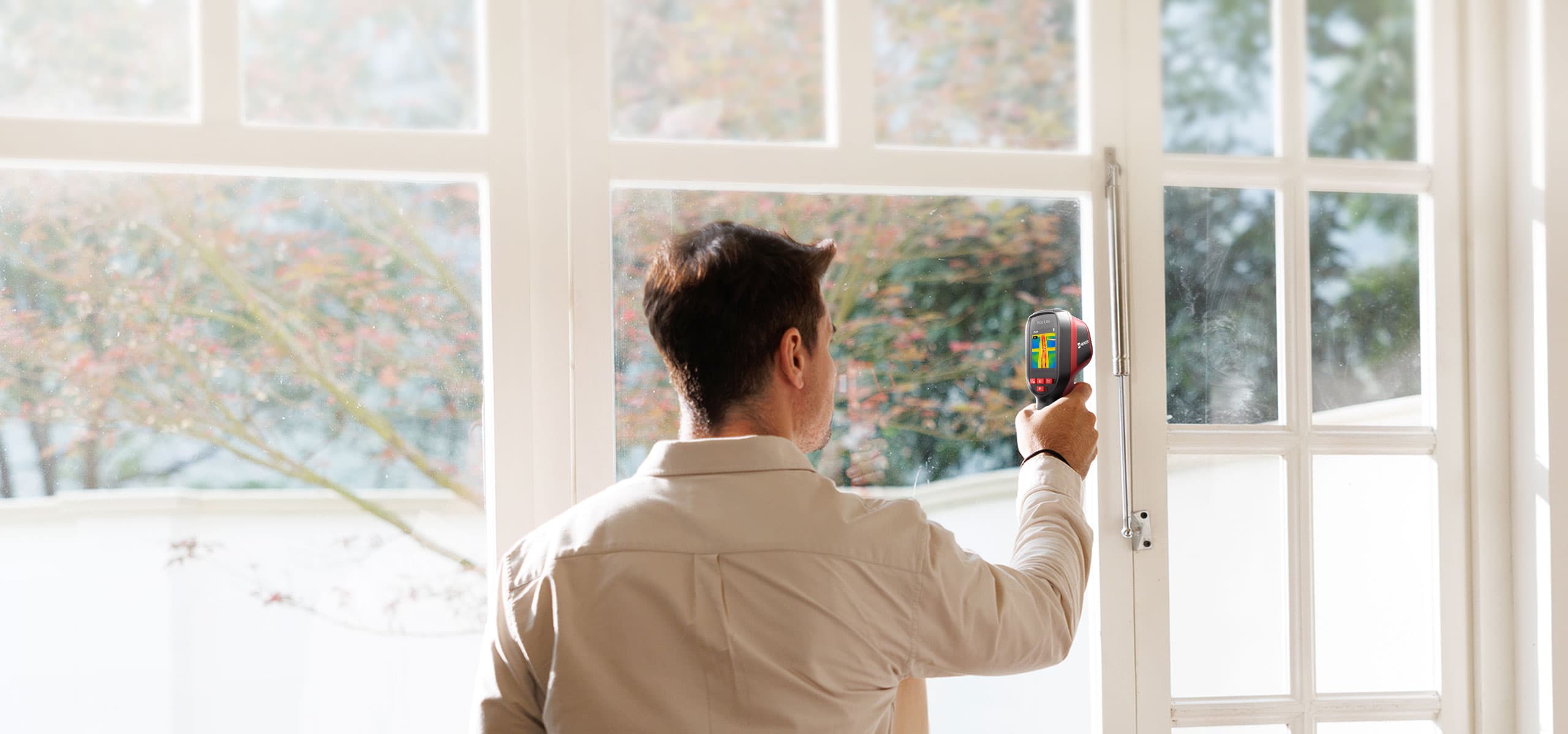 En person använder en värmekamera för att inspektera ett fönster i ett solbelyst rum.