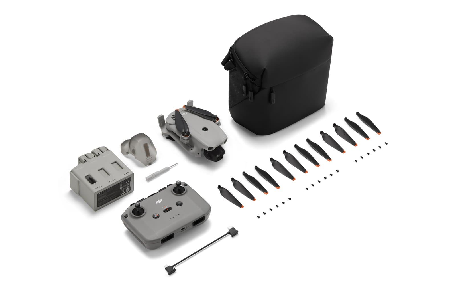 En drönare med tillbehör inklusive fjärrkontroll, propellrar, batteriladdare och en bärväska, arrangerade på en vit bakgrund.