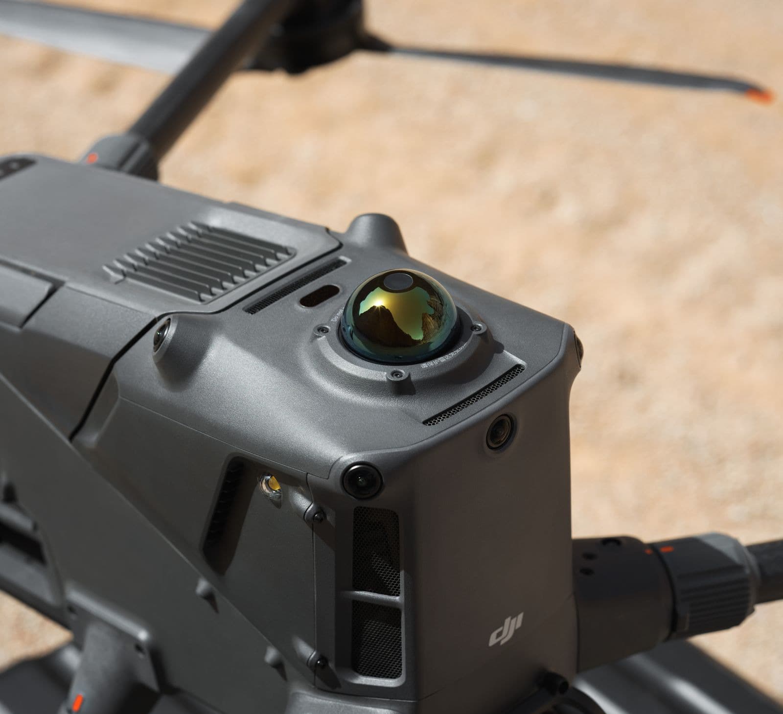 En närbild av en avancerad drönare med en sfärisk sensor, placerad på en grusig yta.