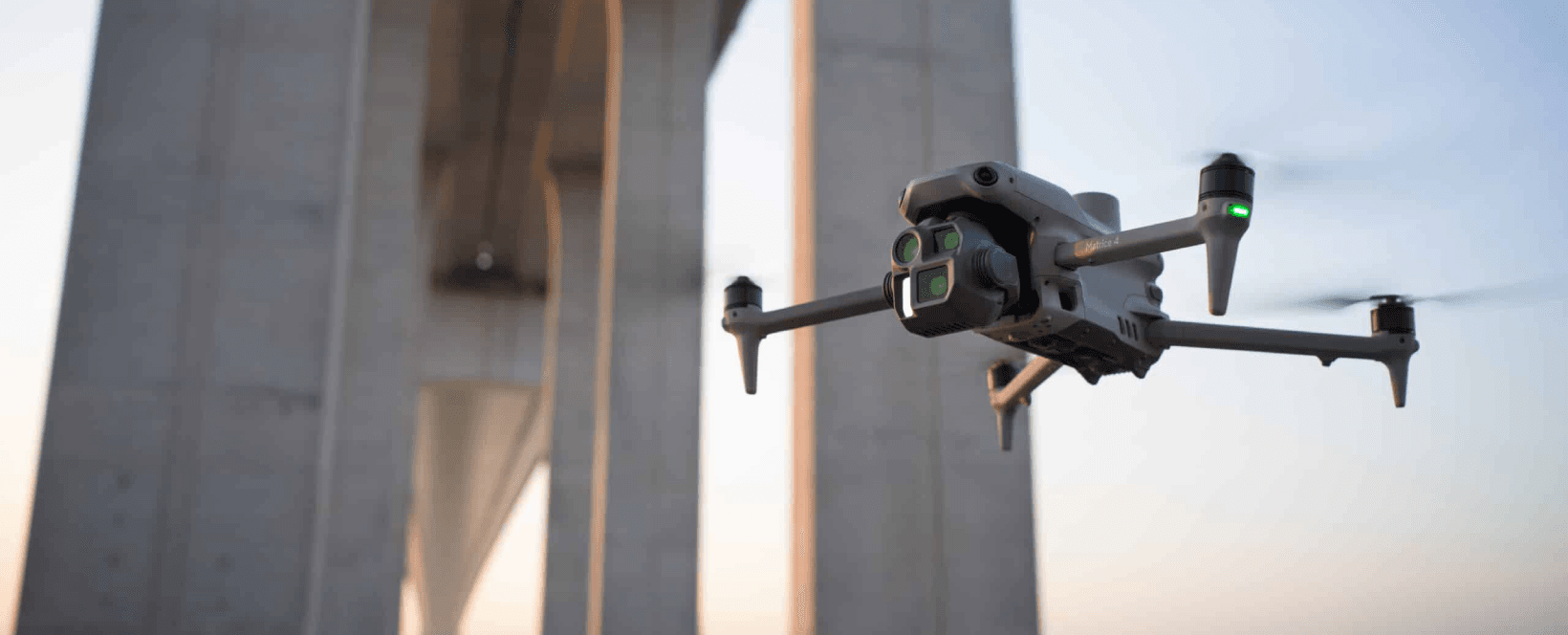 En Matrice 4E-drönare svävar framför en stor betongbro i skymningsljus.