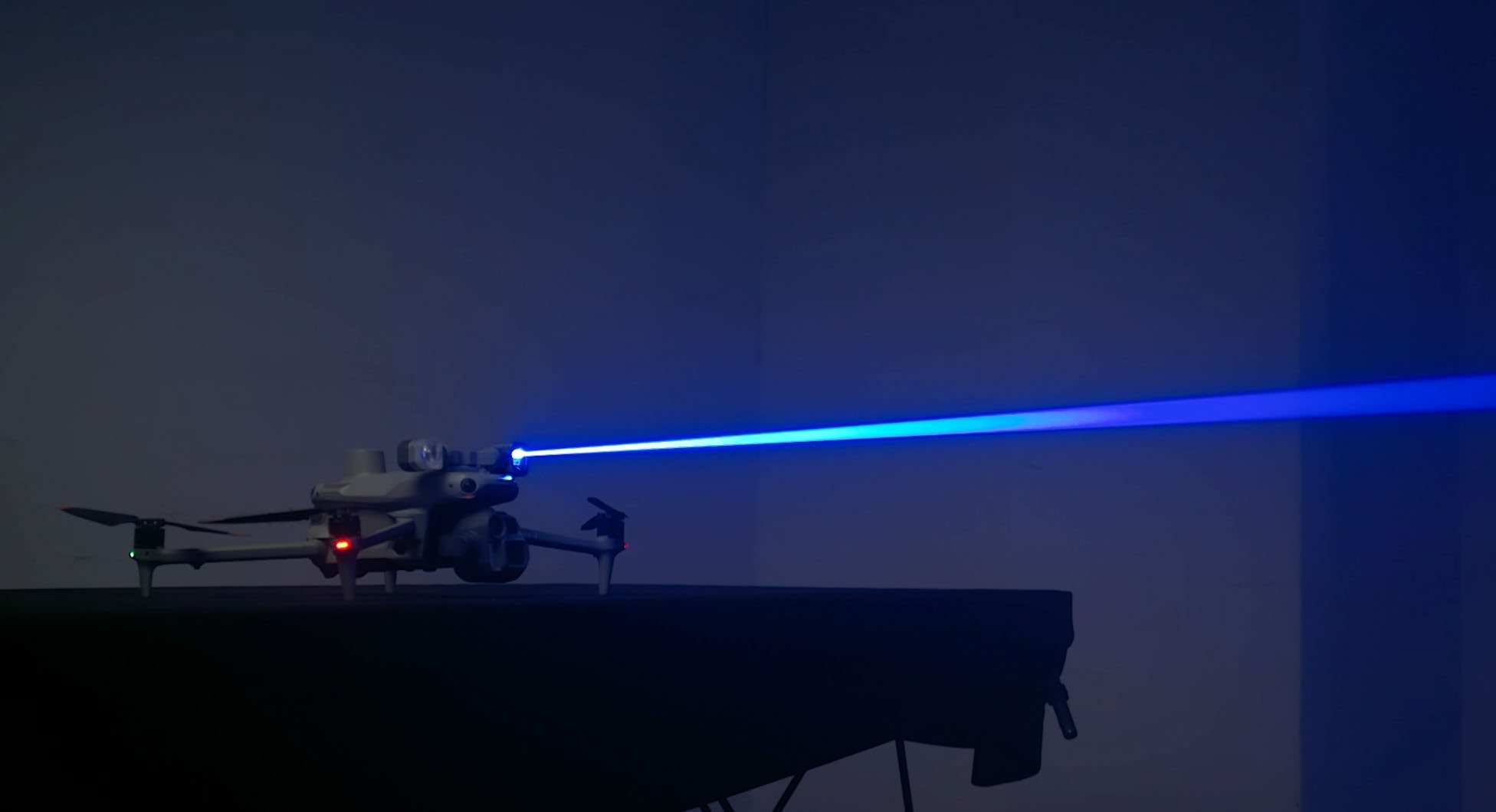 En drönare avfyrar en intensiv blå laserstråle i ett mörkt rum, vilket skapar en futuristisk atmosfär.