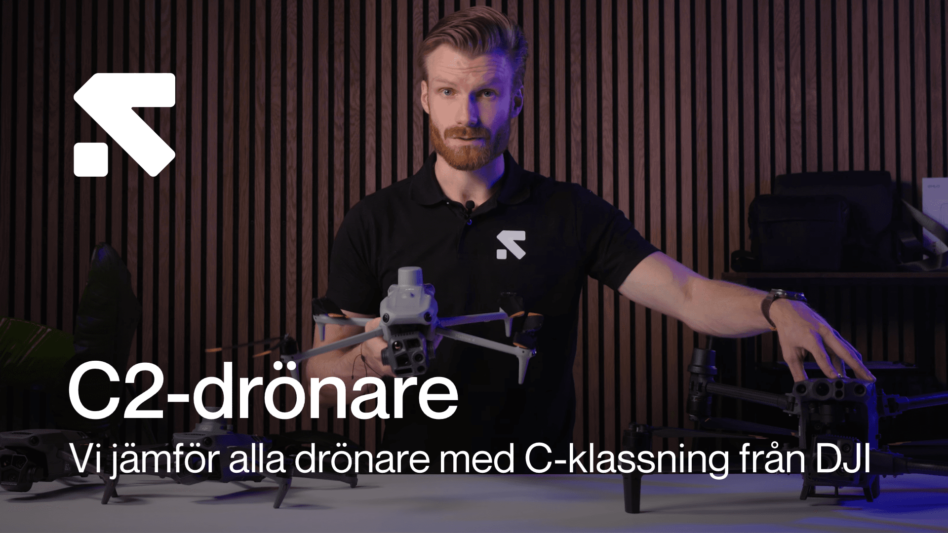 En person presenterar olika C2-klassade drönare från DJI i en studio med träpaneler i bakgrunden.