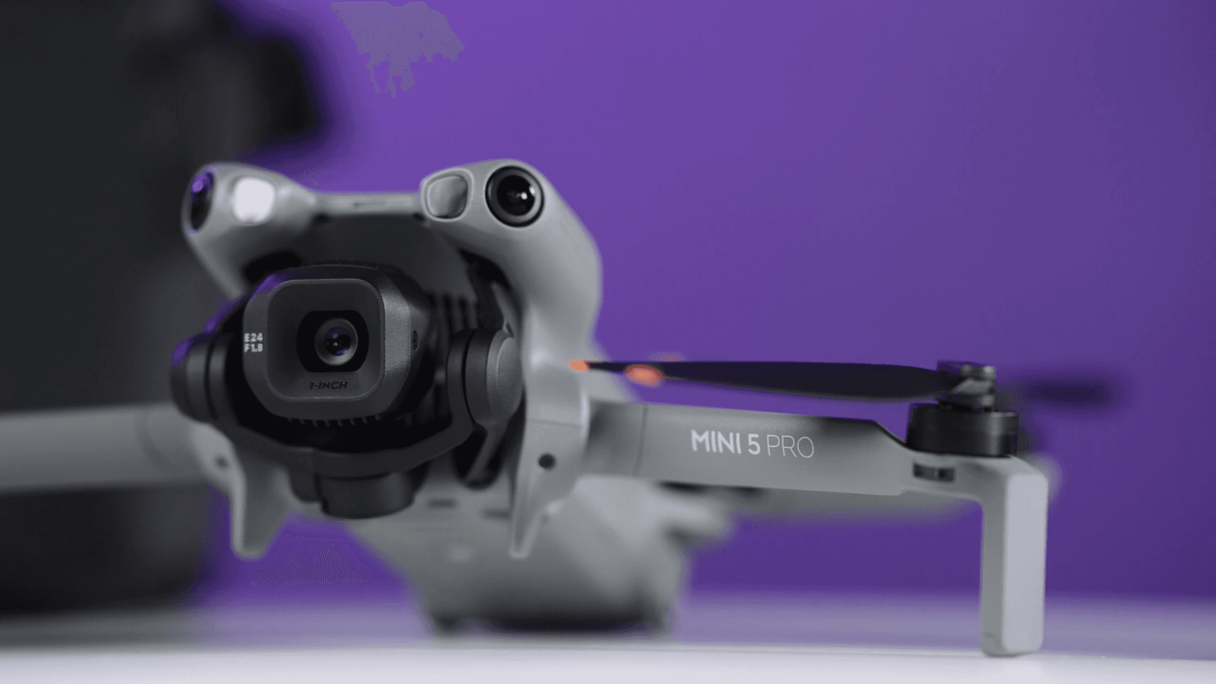 En närbild av en Mini 5 Pro-drönare med en avancerad kamera, mot en lila bakgrund.