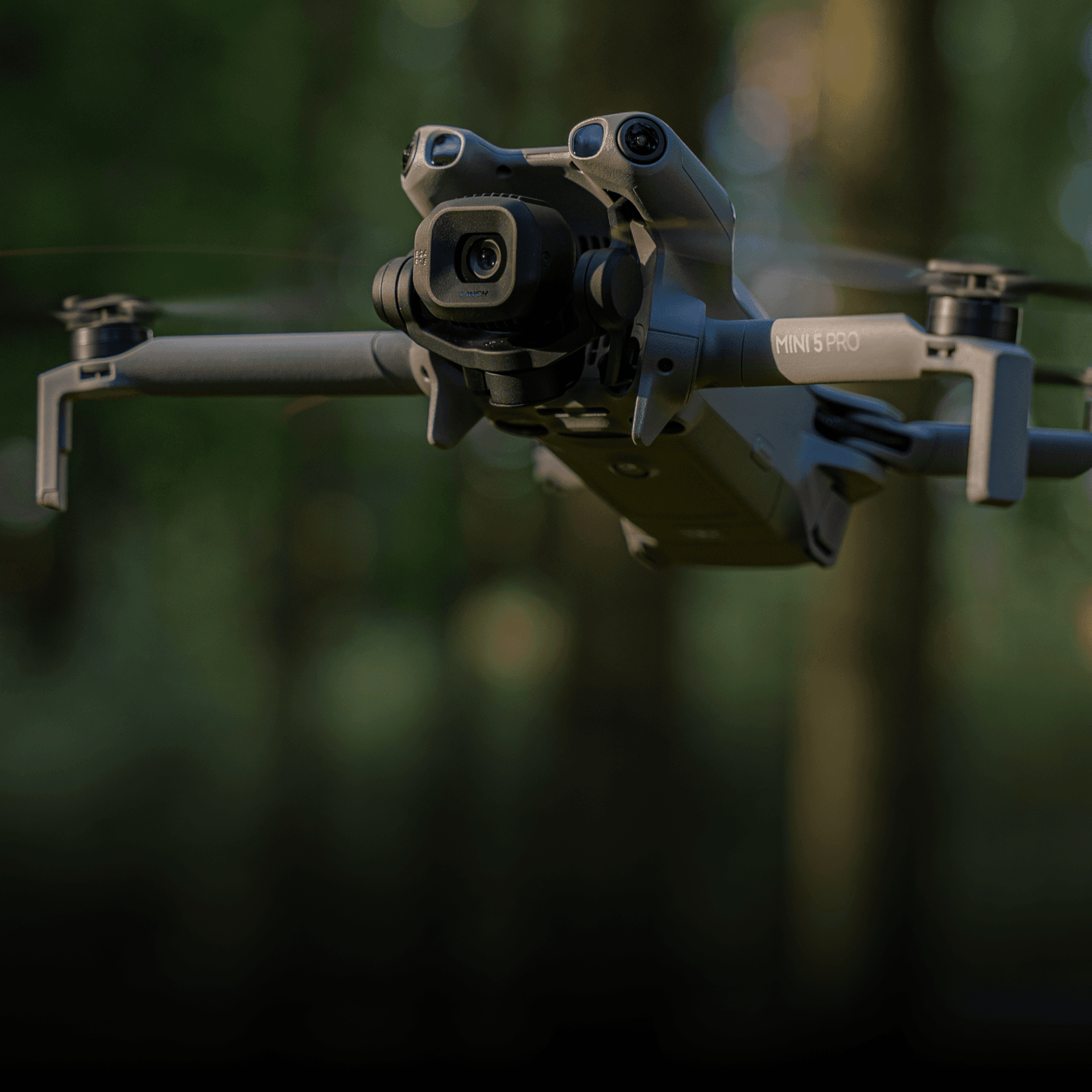 En DJI Mini 5 Pro-drönare svävar genom en skogsmiljö, med fokus på dess avancerade kamera och rotorblad.