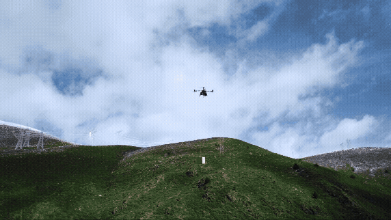 En drönare svävar över en grönskande kulle under en klarblå himmel.