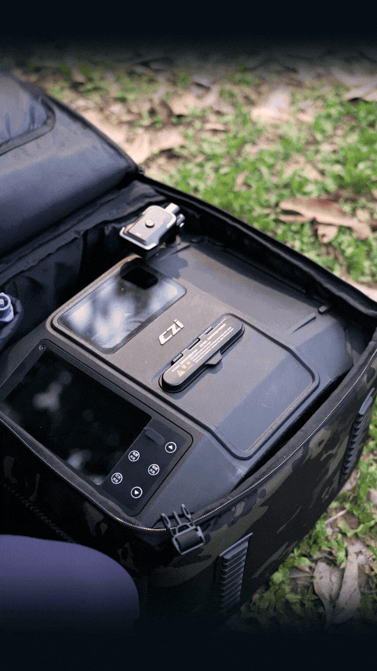 En bärbar drönare packad i en ryggsäck, redo för användning i en utomhusmiljö med gräs och löv.