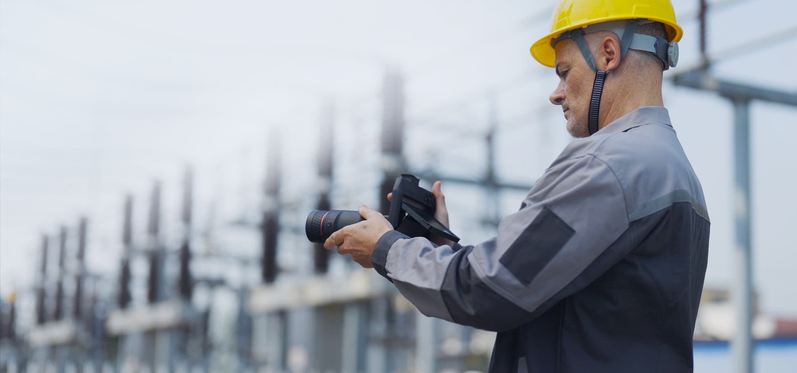 En man i skyddshjälm och arbetskläder använder en kamera för att dokumentera en industriell anläggning.