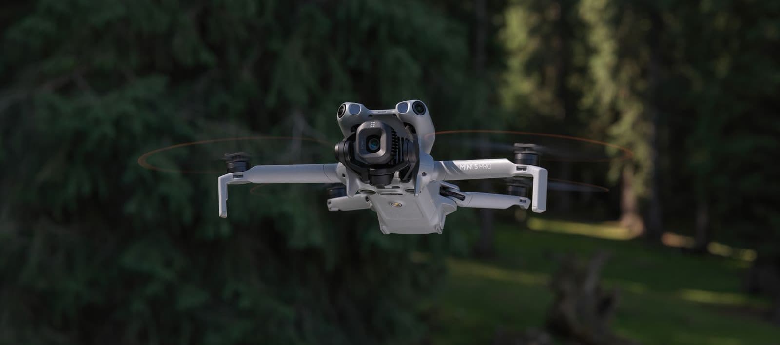 En drönare svävar i luften framför en skog, redo att utforska det gröna landskapet.