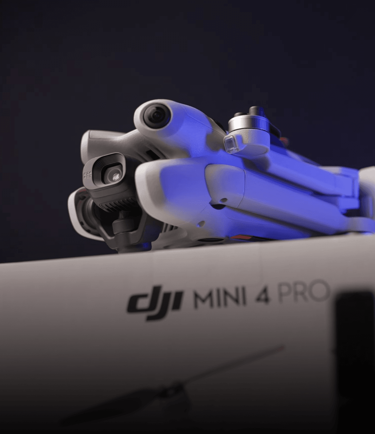 En DJI Mini 4 Pro-drönare visas i närbild, vilande ovanpå sin förpackning mot en mörk bakgrund.
