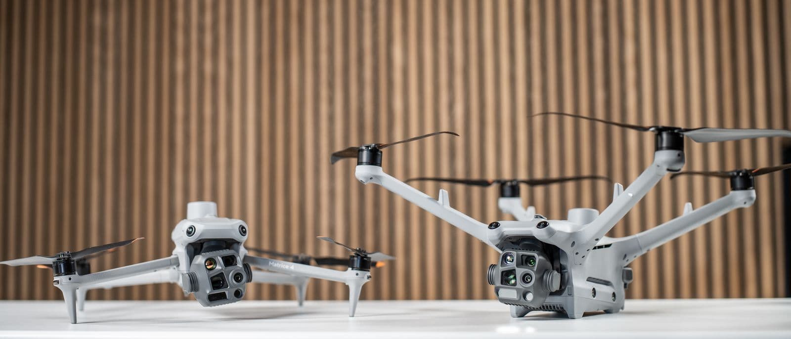 Två avancerade drönare med flera sensorer står på ett bord framför en träpanelvägg. DJI Matrice 4T och DJI Matrice 4TD.