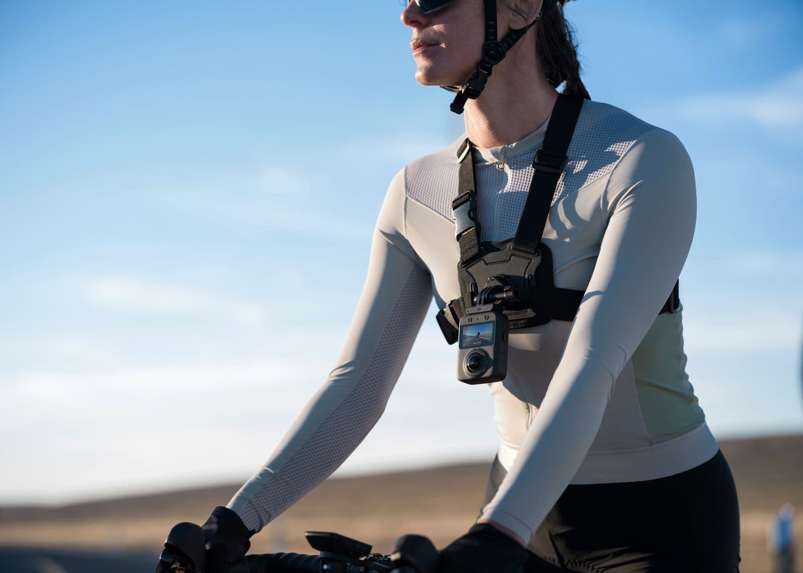 En cyklist med en actionkamera monterad på bröstet cyklar i ett öppet landskap under en klarblå himmel.