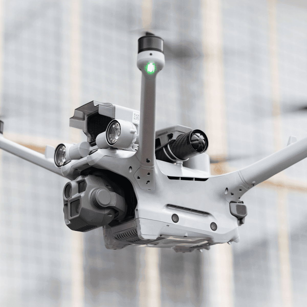 En avancerad drönare med flera sensorer och en grön lysdiod svävar i en inomhusmiljö.