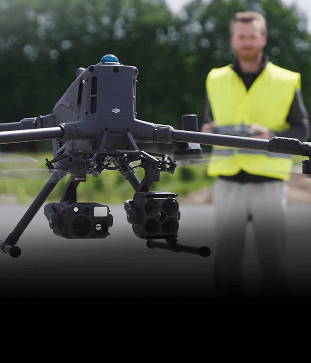 En drönare med avancerad kamerautrustning svävar framför en person i gul väst som styr den med en fjärrkontroll.