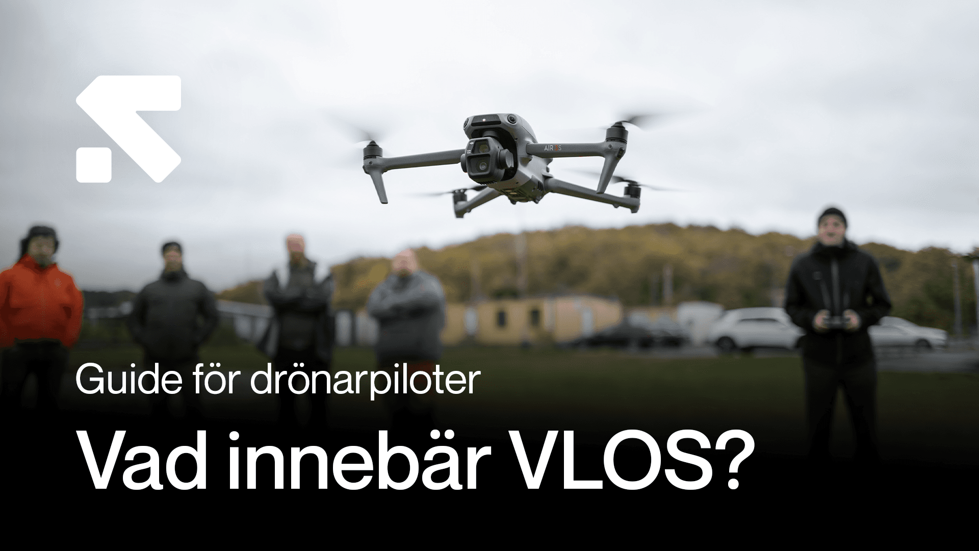 En drönare svävar i luften medan flera personer står i bakgrunden på en gräsyta, med texten 'Guide för drönarpiloter: Vad innebär VLOS?' i förgrunden.