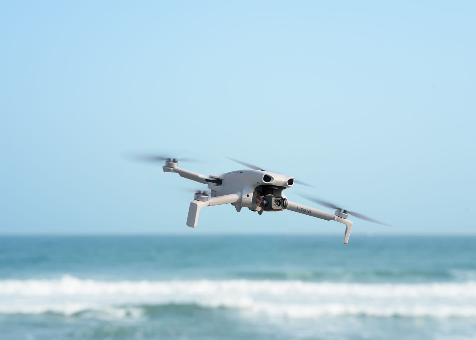 En drönare svävar över en kustlinje med havet i bakgrunden under en klarblå himmel.