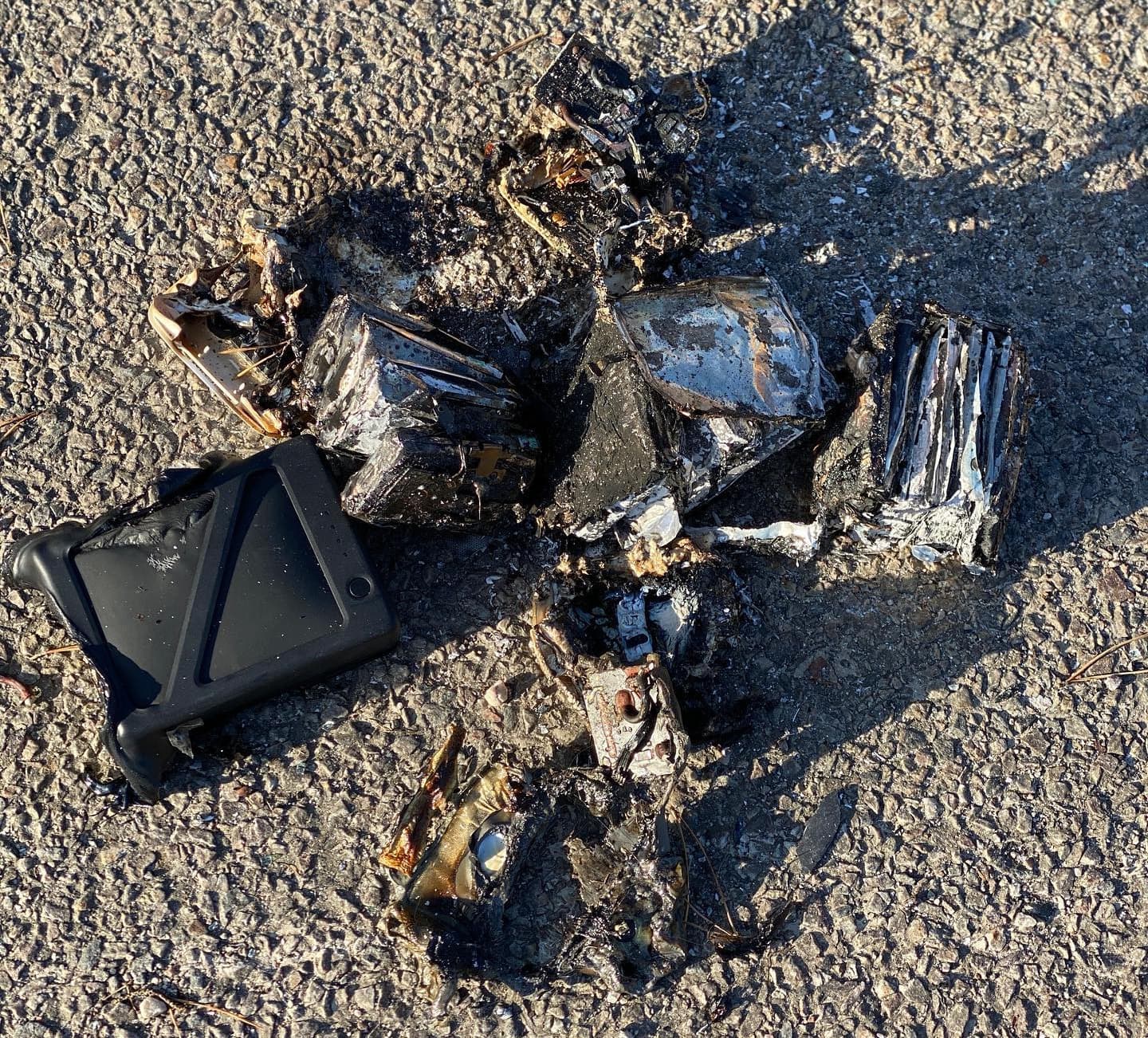 Ett bränt och förstört drönarbatteri ligger på en asfalterad yta, omgiven av rester av ett skyddsfodral.