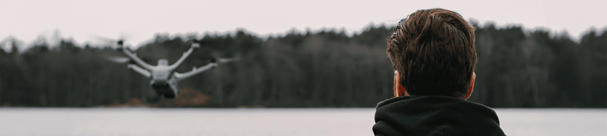 En person i en Swedron-tröja står vid en sjö och observerar en drönare som flyger över vattnet.