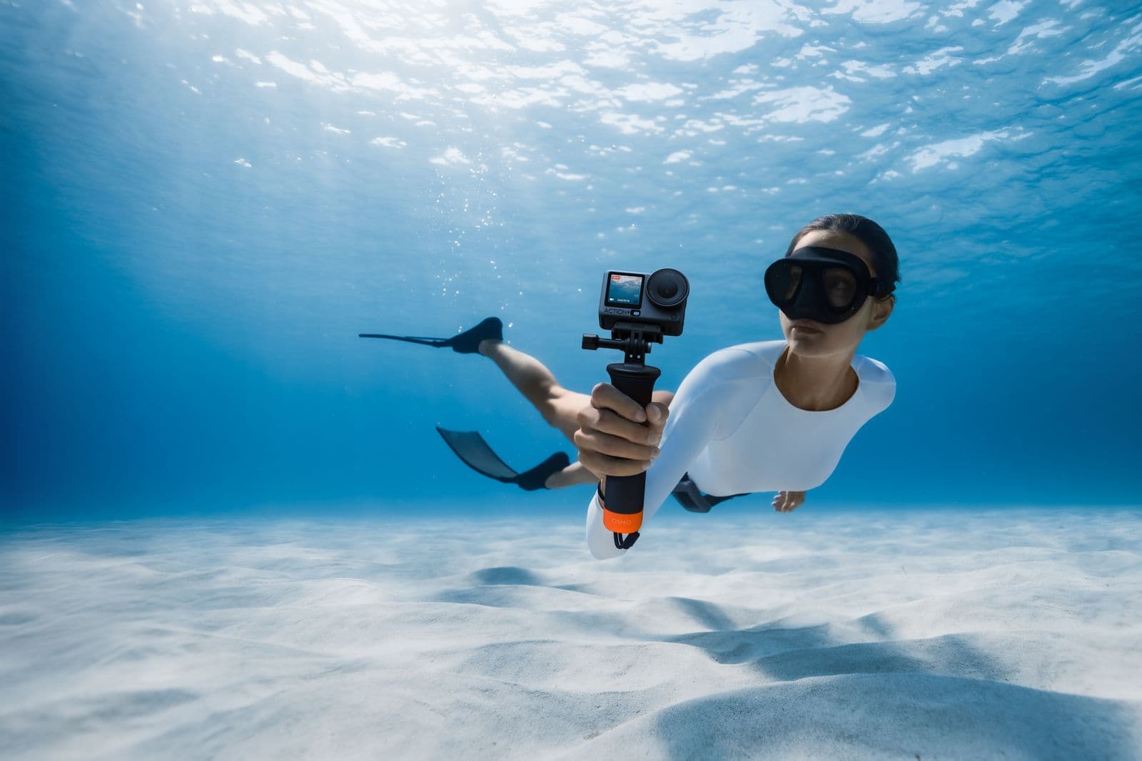 En dykare med simfötter och mask filmar under vattnet med en actionkamera i en klarblå undervattensmiljö.