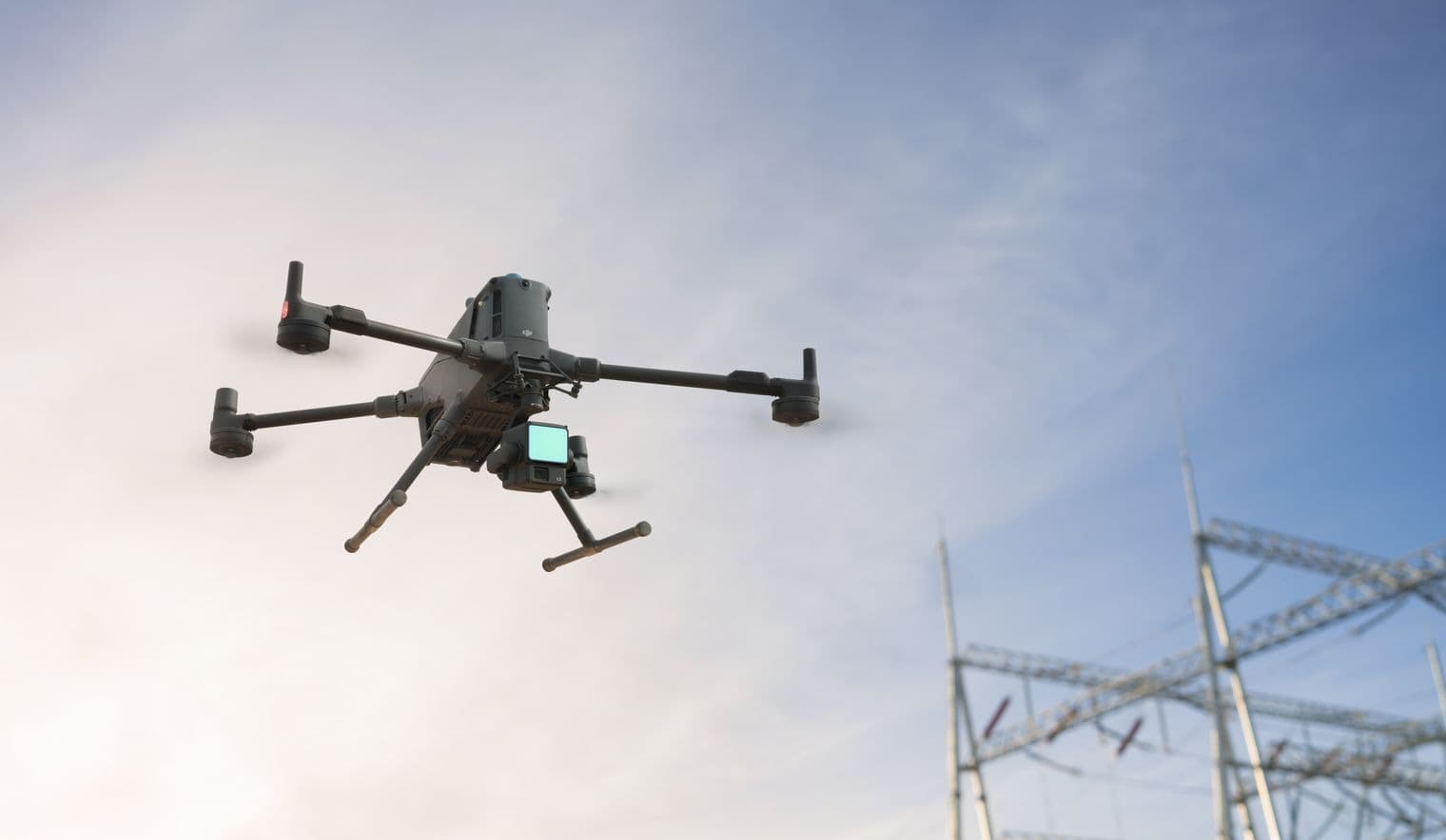 En drönare svävar nära en kraftstation, redo att inspektera elinfrastrukturen mot en klar himmel.