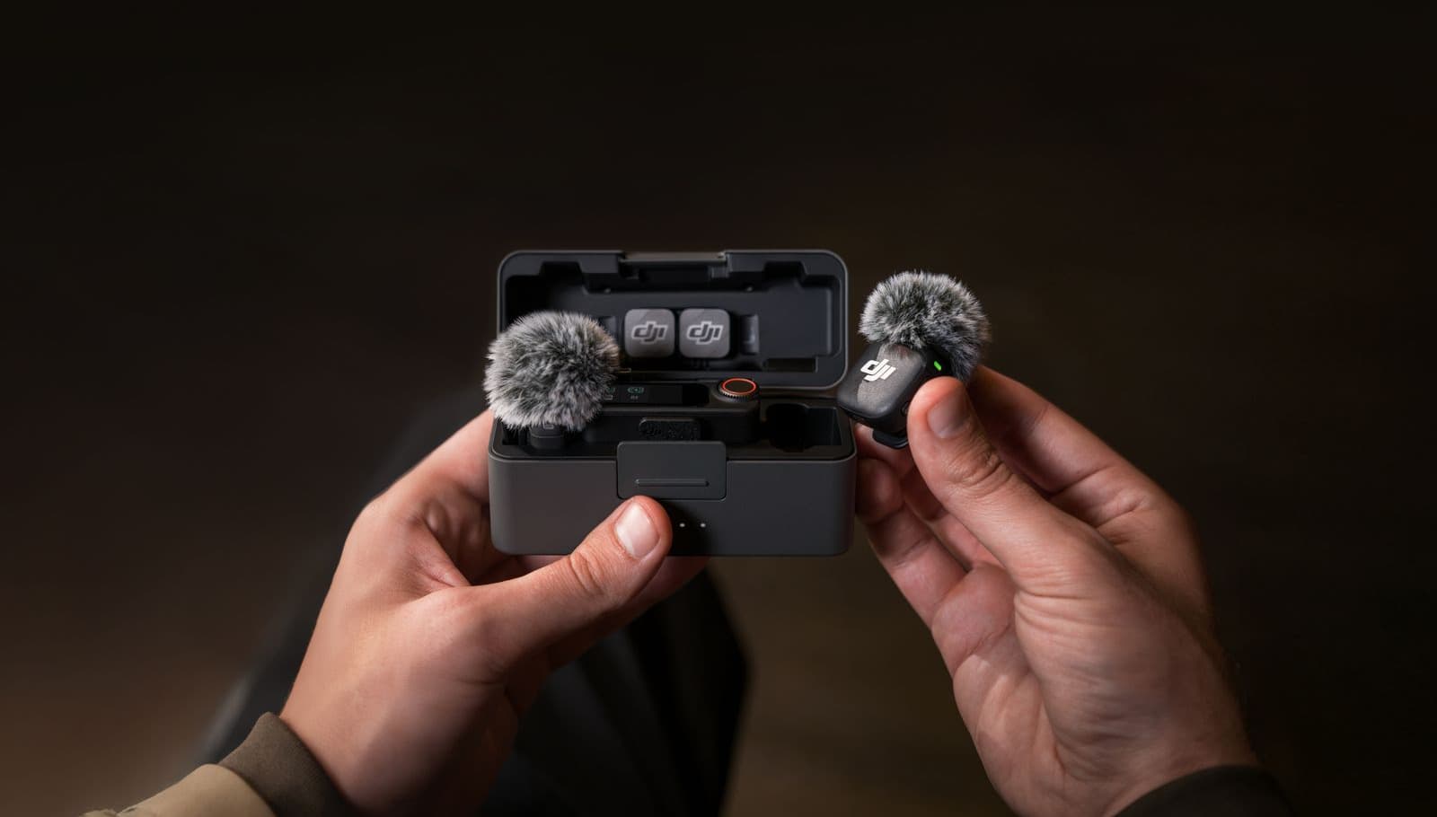 En person håller i en kompakt DJI Mic 3-mikrofon med vindskydd, bredvid ett öppet laddningsetui.