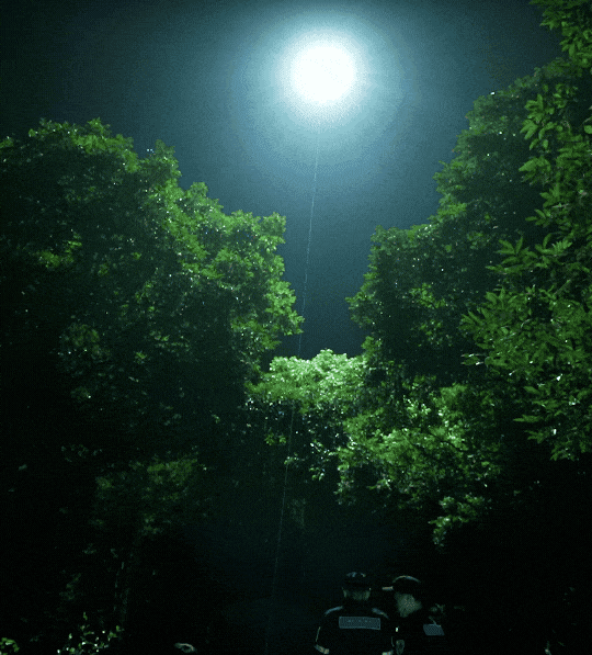 Flera personer i uniform står i en skog under ett starkt ljus som lyser upp natthimlen.