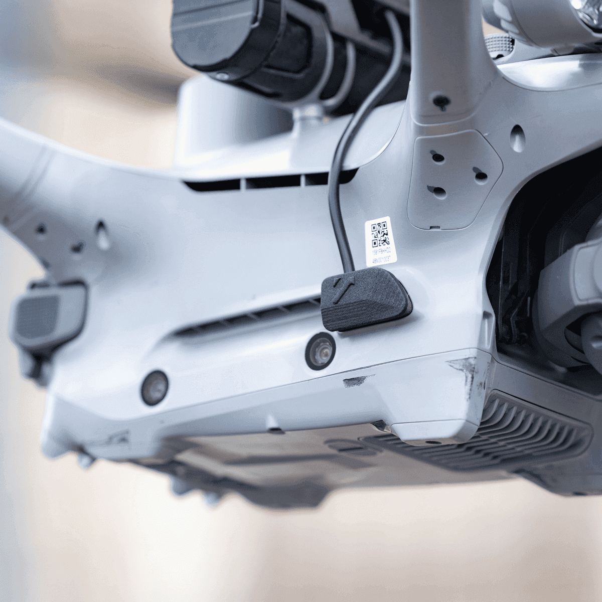 En närbild av undersidan av en drönare med synliga sensorer och en QR-kod.