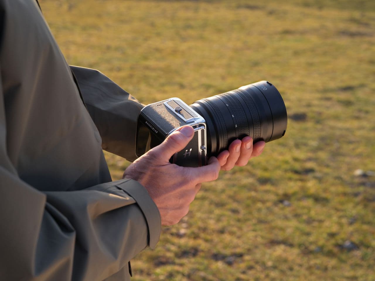 En person håller en avancerad kamera med ett stort objektiv i en solbelyst utomhusmiljö.