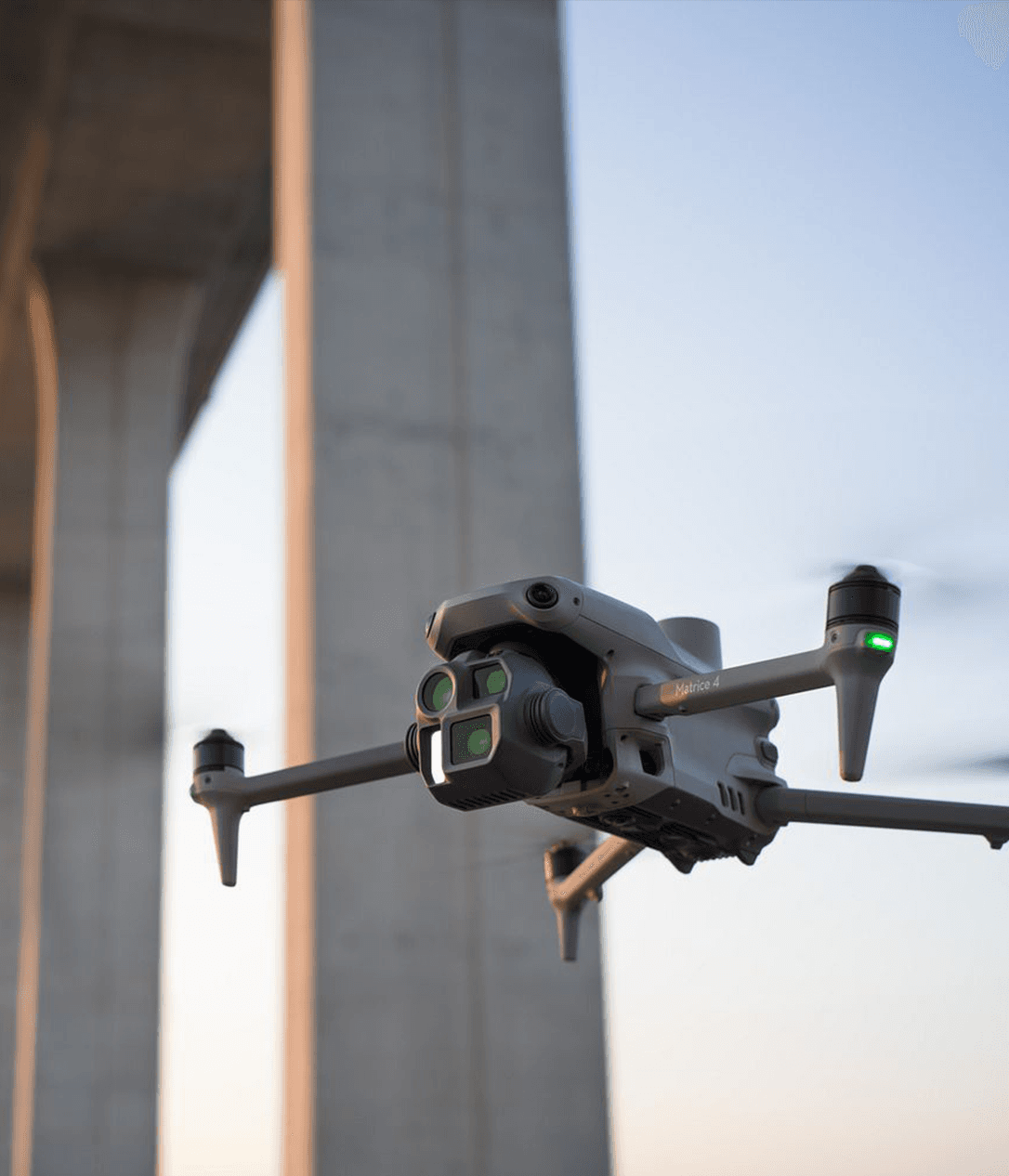 En drönare svävar nära en stor betongstruktur under en klar himmel.