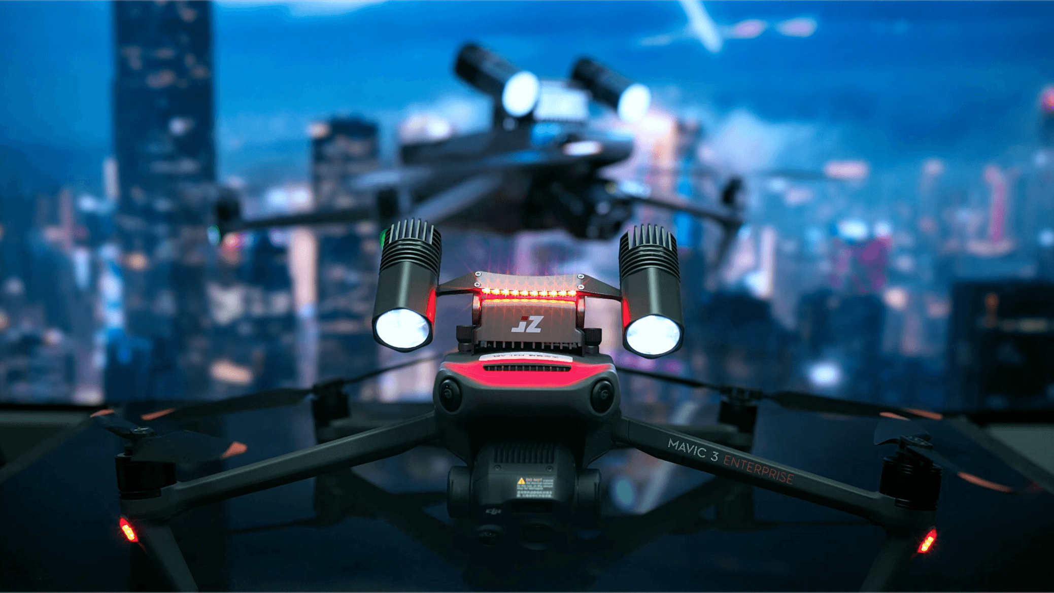 DJI Mavic 3 Enterprise med JLIdrones strålkastare och röda varningsljus framför en upplyst stad