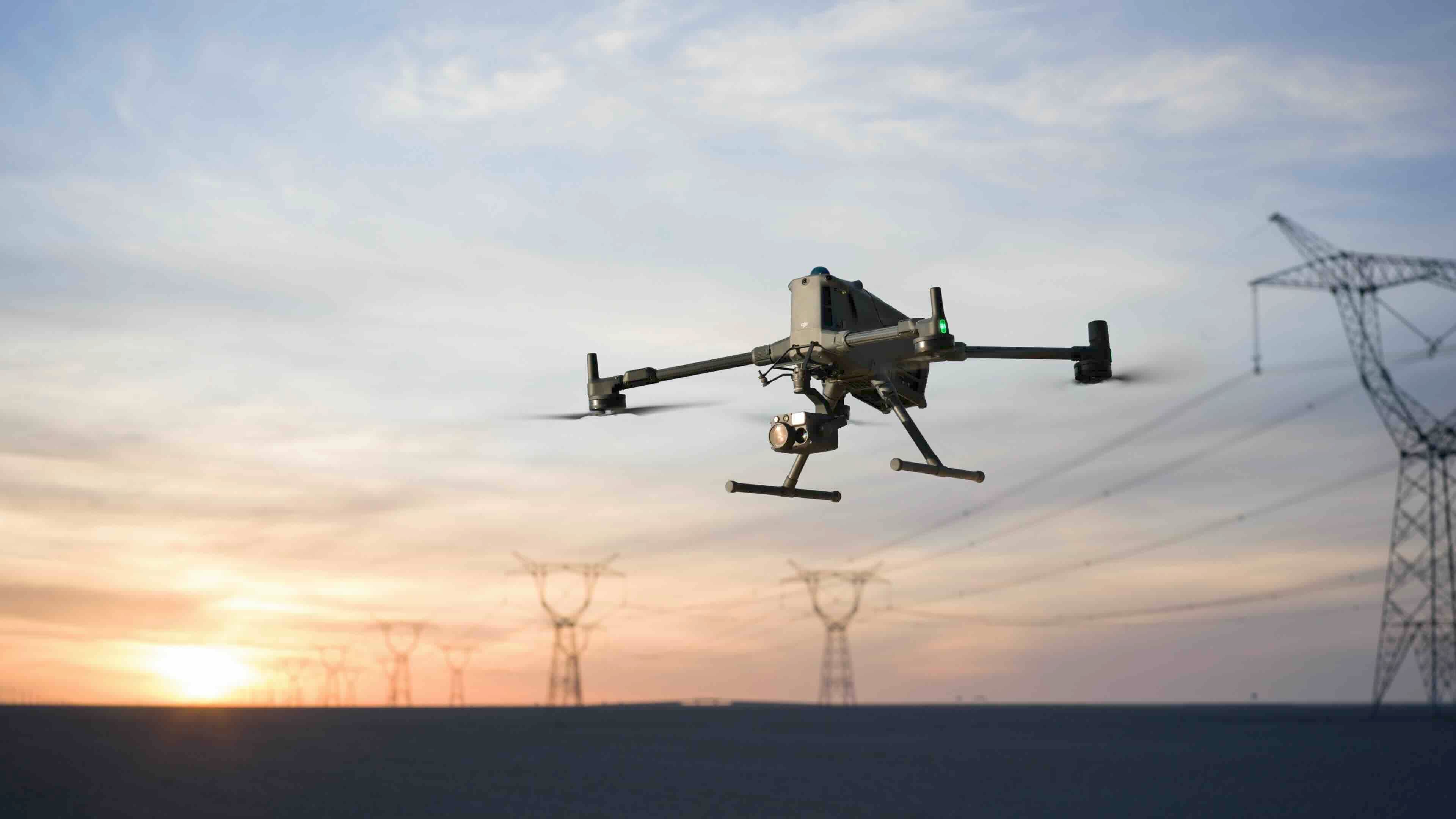 DJI Matrice 400 med kamera flyger i solnedgången framför kraftledningsstolpar