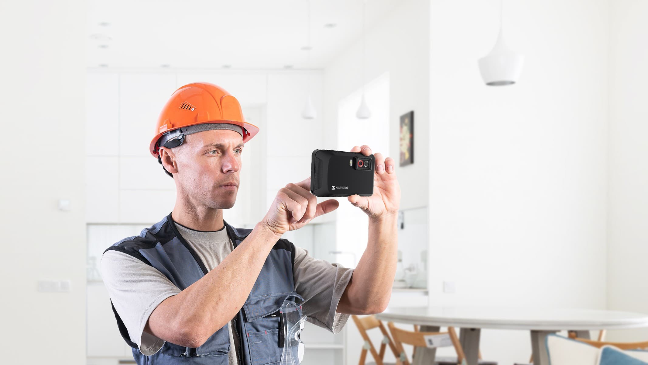 Hantverkare i orange skyddshjälm håller upp en Hikmicro Pocket2 värmekamera inomhus
